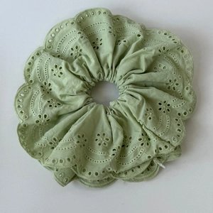 Close-up of light green lace scrunchie with hollow embroidery and scalloped edges