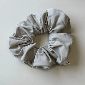 Scrunchie grigio chiaro minimalista con trama verticale ed etichetta del marchio su beige