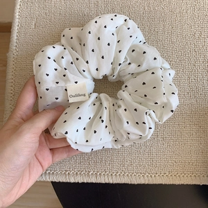 Λεπτομέρεια λευκού scrunchie με μαύρες καρδιές και ετικέτα μάρκας σε κοντινή λήψη