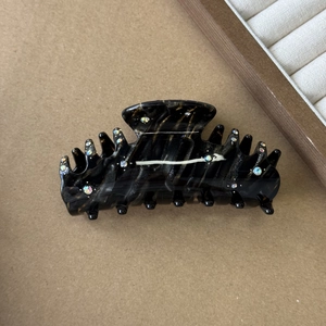 Dettaglio di pinza per capelli tartarugata nera con strass colorati su sfondo marrone