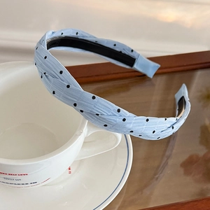 Blue polka dot twisted fabric headband with non-slip teeth shown on a ceramic cup