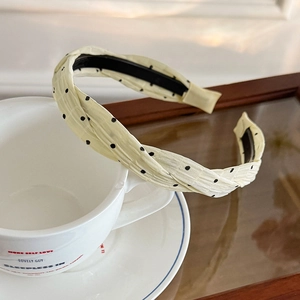Pale yellow polka dot fabric headband with pleated texture on white ceramic cup