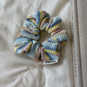 Détail d'un chouchou en maille à rayures colorées posé sur un tissu doux matelassé
