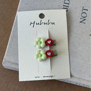 Détail de deux barrettes à fleurs avec strass en cœur sur une carte de présentation