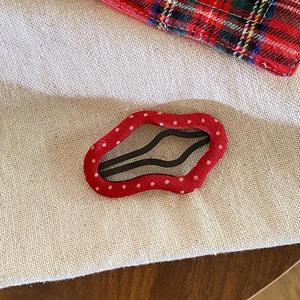 Retro red polka dot fabric hair clip with a wavy design for women on a rustic burlap background