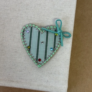 Vue détaillée de la pince à cheveux en tissu rayé vert en forme de cœur avec des strass colorés