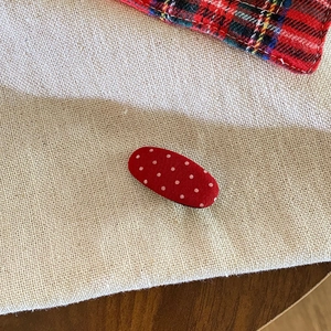 Macro detail of red polka dot fabric hair clip on a minimalist linen texture background