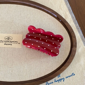 Close-up of retro burgundy hair claw clip with white polka dots on a stylish tray