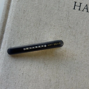 Close-up of black acetate hair clip with 10 inset rhinestones and golden AMY BEAR logo