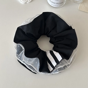 Dettaglio di scrunchie in tessuto nero e mesh a pois bianchi con nastro a strisce