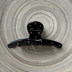 Détail d'une pince à cheveux noire en acétate ornée de strass colorés pour une coiffure élégante