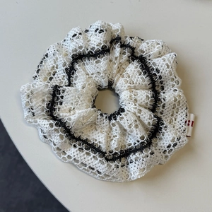 Detailed view of white hollow knit scrunchie with black wavy stitching and textured lace fabric