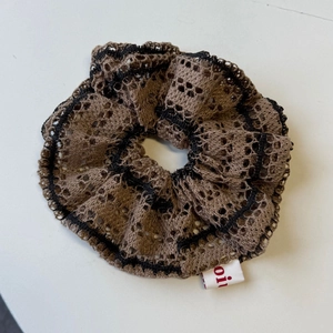 Detail of coffee brown mesh lace scrunchie with black trim and small side tag