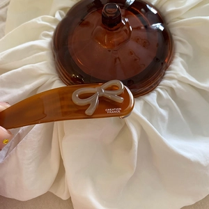 Dettaglio di un fermaglio in acetato marrone con fiocco chiaro e scritta Creation France