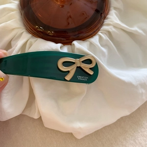 Dettaglio della clip per capelli verde scuro con fiocco beige 3D su sfondo bianco