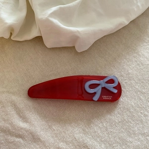 Dettaglio di un fermaglio per capelli rosso a goccia con fiocco lilla su tessuto