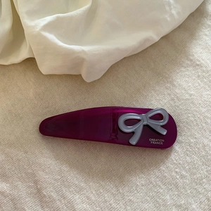 Dettaglio di un fermaglio per capelli in acrilico viola con fiocco grigio e testo francese
