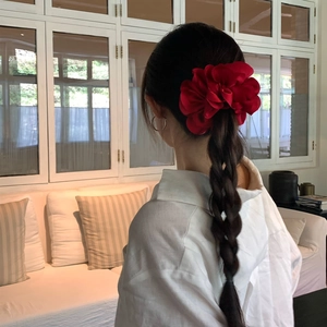 Eleganter roter Blumen-Haargummi aus Stoff an einem Zopf in hellem Wohnambiente