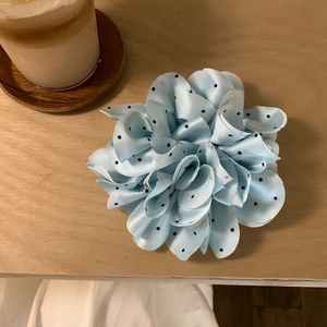 Detail eines hellblauen Satin-Haargummis mit Punkten und Blumenfalten auf Holztisch
