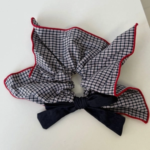 Detail of navy plaid scrunchie with red stitching and a large black ribbon bow