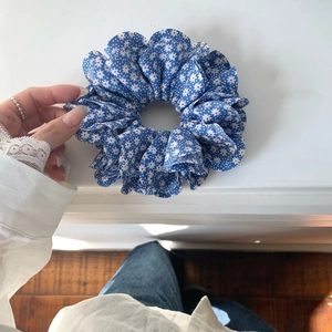 Detailaufnahme eines blauen Blumen-Haargummis mit Gänseblümchen-Muster in der Hand gehalten