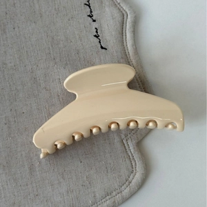Détail d'une grande pince à cheveux couleur crème sur un tissu texturé doux