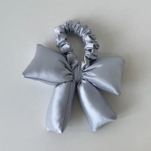 Détail d'un chouchou en satin gris argenté avec nœud rembourré et texture soyeuse