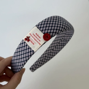 Close-up of plaid fabric headband featuring a vintage red button and cherry pendant detail