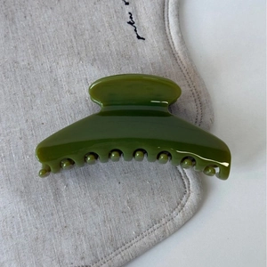 Gros plan sur une pince à cheveux vert olive brillante sur fond de tissu texturé