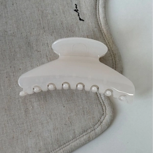 Gros plan d'une pince à cheveux crème brillante sur un tissu en lin beige de style français