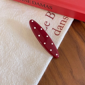 Retro burgundy hair clip with white polka dots displayed on textured beige fabric