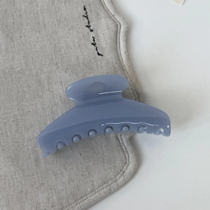 Gros plan d'une pince à cheveux mate bleu brume en acrylique au design incurvé sur lin