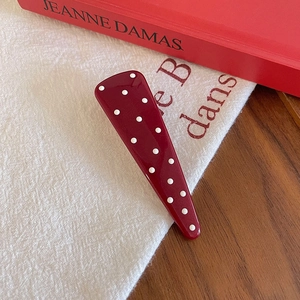 Detailed close-up of a burgundy polka dot hair clip on textured fabric and books