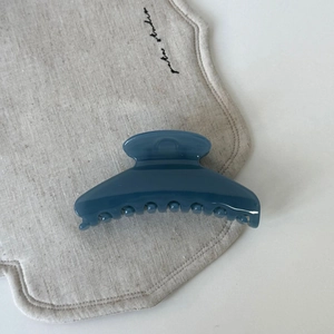 Détail d'une pince à cheveux minimaliste en résine bleu brume sur un tissu en lin beige