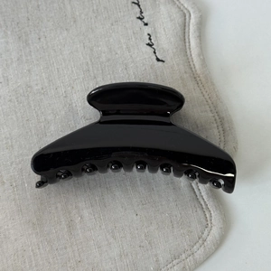 Gros plan d'une grande pince à cheveux noire brillante au design incurvé sur lin