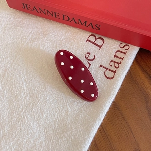 Close-up of a vintage dark red polka dot hair clip on an elegant linen fabric background