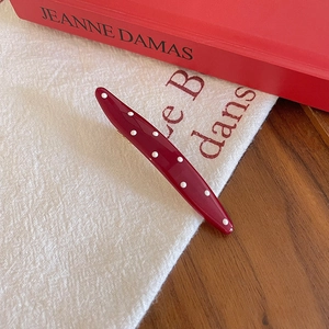 Macro detail of the wine red hair clip with white polka dots and glossy enamel finish