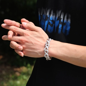 Close-up of a silver iced-out cuban link chain bracelet on a male model wrist