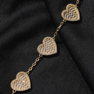 Dettaglio macro del bracciale dorato con cuori, zircone rettangolare e micro-pavé di cristalli
