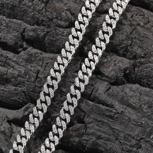 Macro shot of a 6mm silver Cuban link chain with paved moissanite stones on black coal