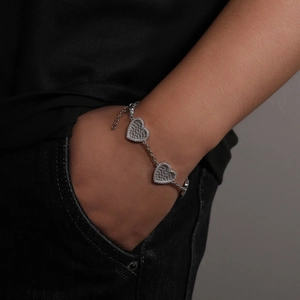 Dettaglio di un braccialetto con ciondolo a cuore e zirconi indossato su jeans neri