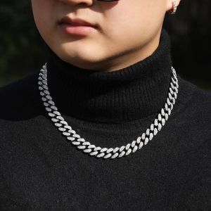 Détail du collier chaîne cubaine argentée avec zircons brillants sur un pull noir