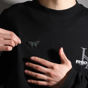Detail einer Schmetterlingsbrosche mit grüner Zirkonia-Einlage auf schwarzem Sweatshirt