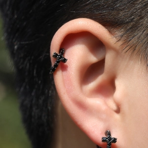 Gros plan d'une boucle d'oreille croix punk noire sertie de zircons 5A sur l'oreille