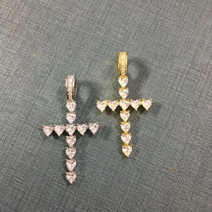 Détail de pendentifs croix en zircon taille cœur argent et or sur fond de tissu gris