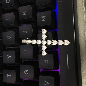 Détail macro du pendentif croix en argent avec zircons en forme de cœur sur fond noir