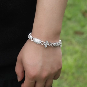 Men's hip-hop silver cross bracelet with evil eye elements worn on wrist outdoors