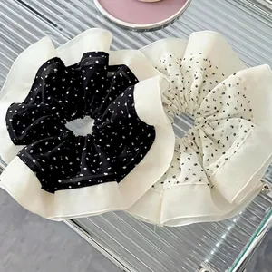 Black and white polka dot large hair scrunchies with white ruffle edges on a glass tray