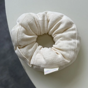 Detail of a creamy white knitted scrunchie with pointelle hollow patterns and fabric label