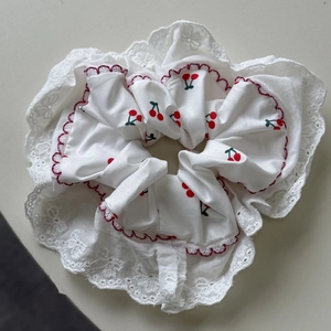 Detail of white scrunchie featuring cherry embroidery and delicate lace trim edges